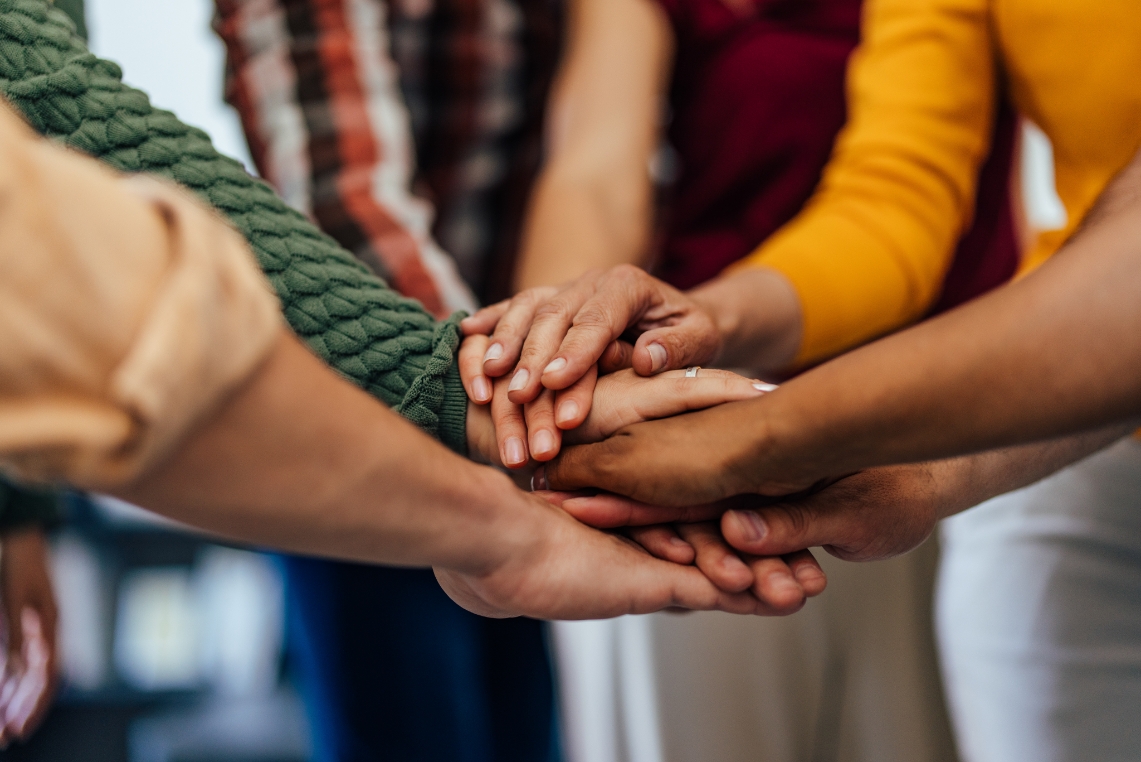 Many hands piled on top of each other in a team circle.