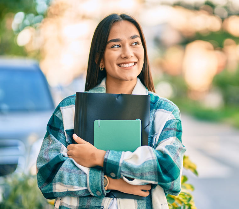 Young, pretty hispanic student holding her schoolbooks and smiling outdoors.